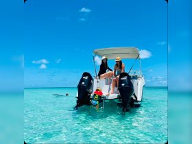 A joyful family enjoys a sunny day on the water, with one child playfully climbing onto the boat while adults relax — a perfect snapshot of summer fun and adventure.