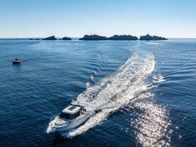 A stunning aerial view of a speedboat cruising through calm waters, leaving a shimmering wake behind as it approaches rocky islands in the distance.