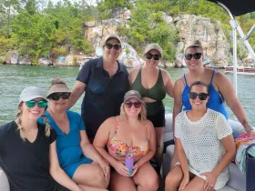 A cheerful group of friends enjoys a day on the water, capturing memories aboard a boat with a scenic rocky backdrop — perfect for summer celebrations and gatherings.