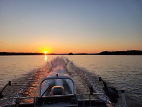 A serene sunset view from the back of a boat, showcasing the tranquil waters and beautiful reflections — perfect for evening cruises.