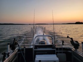 A scenic view from the back of a fishing boat cruising at sunset, showcasing the tranquil waters and the boat's wake — perfect for fishing enthusiasts and sunset lovers.