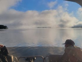 A serene morning scene on the water with fog rolling over the lake, showcasing guests enjoying the tranquil atmosphere aboard a boat.