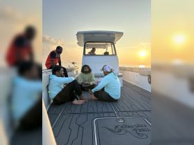 A group of friends relaxes on the deck of a boat during sunset, enjoying a moment of camaraderie on the water.