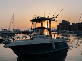 A fishing boat silhouetted against a stunning sunset, showcasing its structure and equipment while docked in a serene harbor.