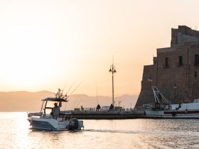 A fisherman navigates his boat through a picturesque harbor at sunset, capturing the essence of a tranquil evening on the water.