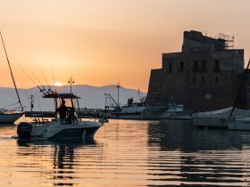 A fishing boat navigates through a tranquil harbor at sunset, creating a picturesque scene perfect for evening excursions and fishing adventures.