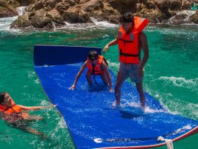 A lively group enjoys a fun water activity on a floating mat, showcasing the excitement of summer adventures in crystal-clear waters.