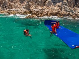 A group enjoys a fun water activity in vibrant turquoise waters, showcasing the excitement of swimming and playing on a floating mat.