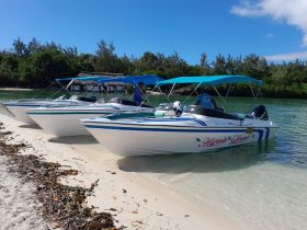 A fleet of speedboats, including 'Aqua Love,' docked on a sandy beach, showcasing the perfect setup for a day of water adventures.