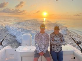 Two friends enjoy a beautiful sunset while fishing on a boat, creating the perfect backdrop for a memorable day on the water.