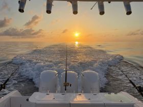A stunning sunset view from the back of a fishing boat, showcasing the tranquil ocean waters and the excitement of a fishing adventure.