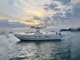 A picturesque side view of the 'Mathis' boat cruising in calm waters at sunset, showcasing its sleek design against a stunning sky.