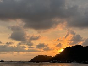A stunning sunset over a tranquil harbor, showcasing various boats anchored along the coastline — a picturesque scene perfect for evening cruises.