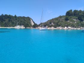 A serene view of a sailboat anchored in crystal-clear turquoise waters, surrounded by lush greenery and rocky cliffs — an ideal setting for a peaceful getaway.