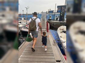 A father and his young child stroll along the marina, hand in hand, creating cherished family memories by the water.