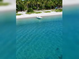 Aerial view of a speedboat anchored near a pristine beach, surrounded by clear turquoise waters and lush palm trees — an ideal setting for a relaxing day on the water.