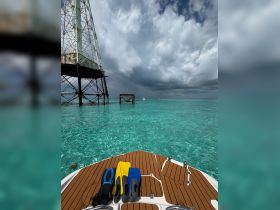 A vibrant view of snorkeling fins resting on the deck of a boat, with a stunning turquoise backdrop and a distant boat in sight — perfect for underwater adventures.