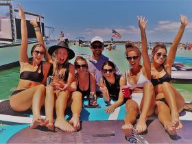 A lively group of friends enjoys a fun day on the water, celebrating with drinks and laughter while lounging on a paddleboard.