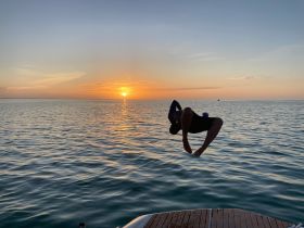 A person leaps into the water at sunset, capturing the thrill of summer adventures on the water — perfect for those seeking unforgettable experiences.
