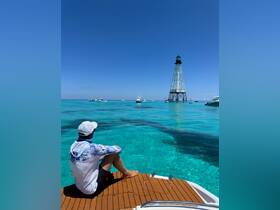 A man enjoys the stunning view of a lighthouse while sitting on the deck of a boat, surrounded by crystal-clear turquoise waters — a perfect moment for relaxation and sightseeing.