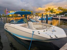 A sleek speedboat docked in calm waters, showcasing its stylish design and vibrant colors against a picturesque backdrop of palm trees and a sunset sky.