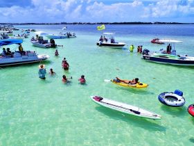 A vibrant scene at a sandbar with groups of people enjoying swimming and kayaking among various boats — a perfect day for water activities and fun in the sun.