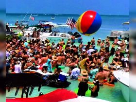 A vibrant beach party scene filled with people enjoying the sun and water, showcasing the ultimate summer fun with boats in the background.