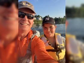 A joyful selfie of a father and son enjoying a day on the water, both wearing life jackets — a perfect moment for family bonding while boating.