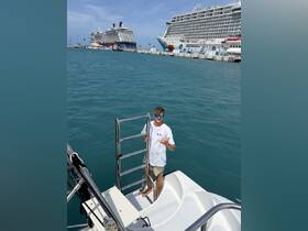 A young man poses with a friendly gesture on the deck of a boat, with cruise ships visible in the background, capturing the excitement of a day on the water.