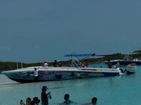 A lively scene at Exuma with guests enjoying the water around a colorful boat, capturing the essence of fun and adventure in the Bahamas.