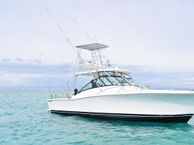 A sleek fishing yacht navigates through clear turquoise waters, showcasing its impressive design and fishing equipment.