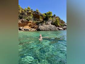 A snorkeler enjoys the crystal-clear waters, surrounded by stunning rocky cliffs and lush greenery — a perfect spot for underwater exploration.