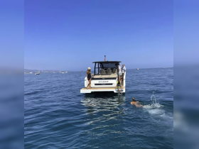 A lively scene with guests enjoying a summer day on the water, with one person swimming and others relaxing on the boat. Perfect for showcasing fun boating experiences.