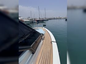 A close-up view of a yacht's exterior at the dock, showcasing its sleek design and wooden deck, with other boats visible in the marina.