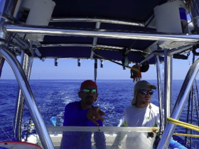 Two crew members are seen at the helm of a fishing boat, navigating the open waters. The interior setup highlights the boat's operational features.