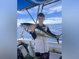 A young boy proudly holds up a large tuna while fishing on a boat, showcasing the thrill of a successful catch on the open water.