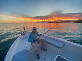 A fisherman enjoys a serene sunset while casting his line from a boat, capturing the essence of a perfect fishing trip on the water.