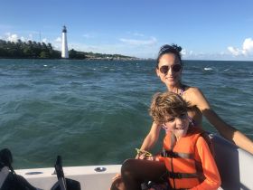 A joyful moment captured on a boat with a mother and her son, enjoying the ocean breeze with a lighthouse in the background — perfect for family adventures on the water.