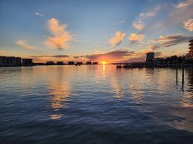 A stunning sunset reflects on calm waters, showcasing the beautiful coastline and buildings along the shore — a perfect backdrop for evening boat trips.
