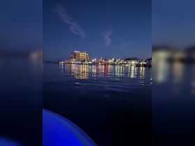 A serene night view of a vibrant waterfront city, with colorful lights reflecting on the calm water — perfect for evening boat tours and city explorations.