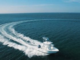 An aerial view of a speedboat named 'FIRST SHOT' making sharp turns in open water, showcasing its agility and performance on the waves.