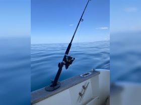 A fishing rod is set up on the side of a boat, ready for a day of fishing on calm waters — perfect for anglers looking to catch their next big fish.