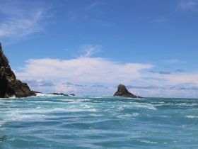 A stunning view of rocky formations rising from the ocean under a bright blue sky, showcasing the natural beauty of the coastline.