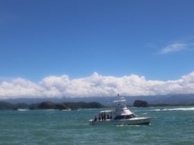 A fishing boat navigates through vibrant ocean waters, showcasing a scenic backdrop of lush islands and dramatic clouds — perfect for adventure seekers and fishing enthusiasts.
