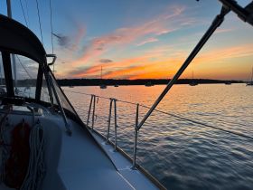 A stunning sunset view from the deck of a yacht, showcasing the tranquil waters and anchored boats in the background — perfect for evening cruises.