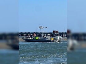 A man stands on a boat near a pier, enjoying a sunny day on the water, perfect for fishing or leisure activities.