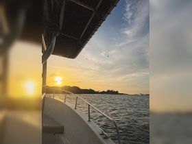 A stunning sunset view from the bow of a boat, showcasing the tranquil waters and distant shoreline — perfect for evening cruises.