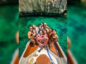 A vibrant group of friends enjoys a fun day on the water, celebrating with drinks and a heart-shaped float on their boat — perfect for summer adventures and memorable outings.