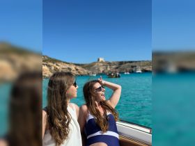 Two friends enjoy a sunny day on a boat, showcasing the vibrant turquoise waters and stunning coastline — perfect for summer adventures and memorable outings.