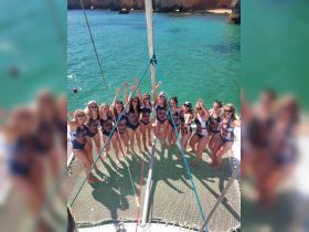 A lively group of friends celebrates aboard a catamaran, showcasing their unique swimsuits and enjoying a fun day on the water.